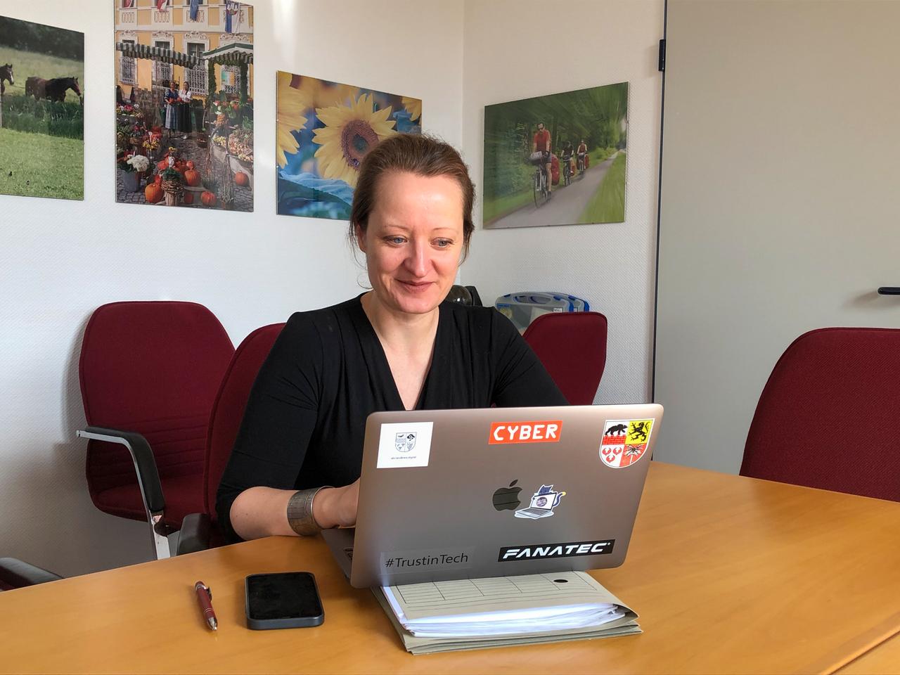 Eine Frau sitzt am Laptop und schaut freundlich.