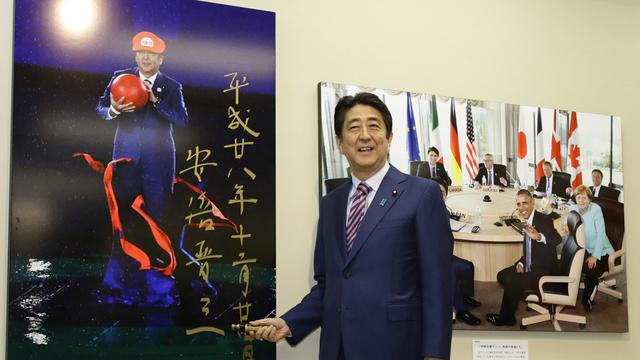 Japans damaliger Premierminister Shinzo Abe posiert vor einen Foto, welches ihn als "Super Mario" während der Schlussfeier der Olympischen Sommerspiele in Rio 2016 zeigt. 
