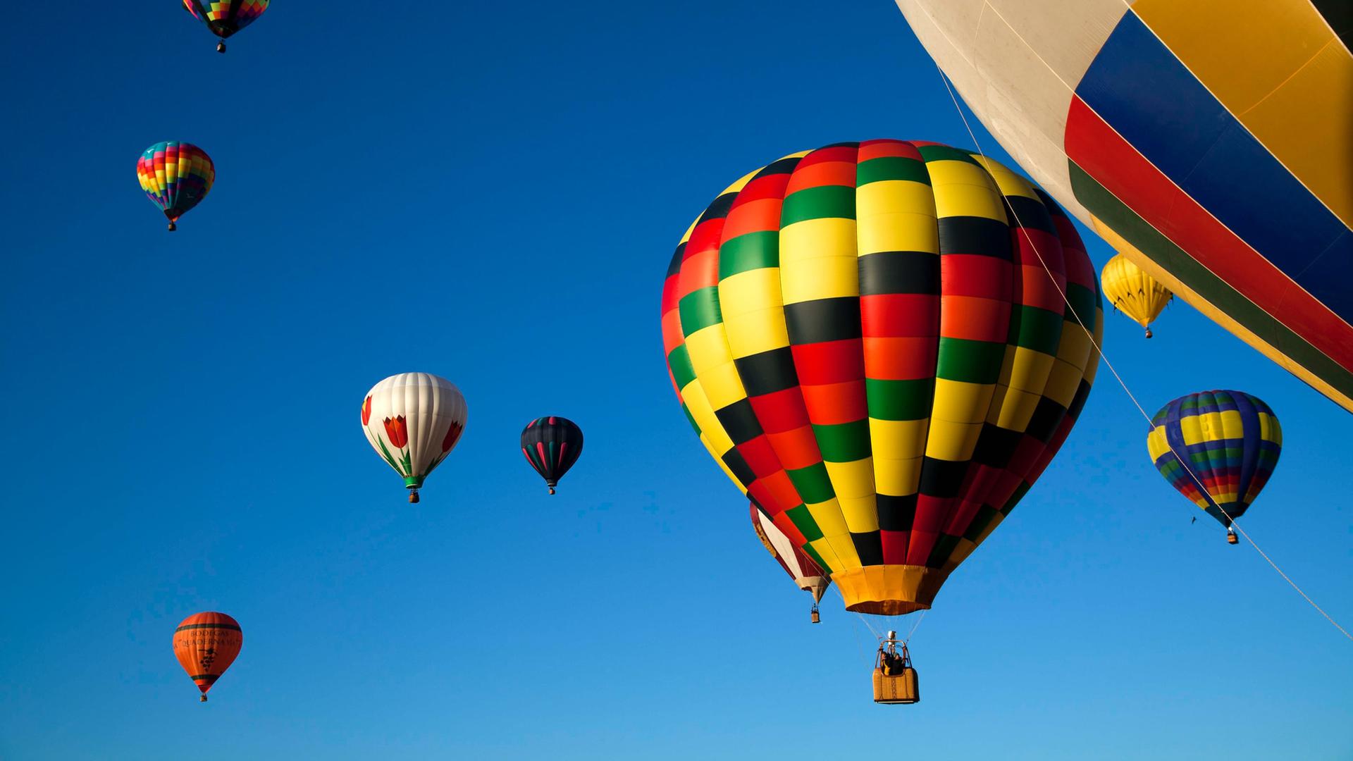Mehrere bunte Heißlufballons sind vor einem klaren, hellblauen Himmel zu sehen. Mehrere bunte Heißlufballons sind vor einem klaren, hellblauen Himmel zu sehen.