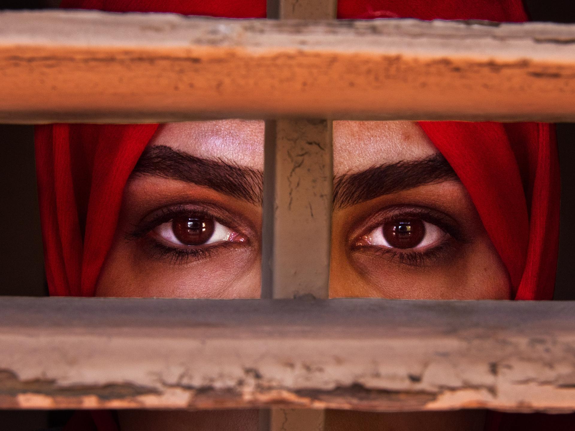 Eine afghanische Frau blickt durch ein vergittertes Fenster 