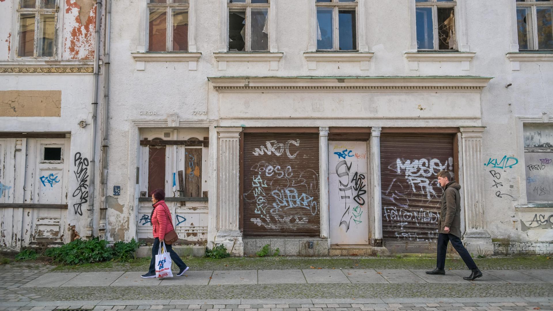 Zwei Menschen laufen an einer Hausruine im Landkreis Ostprignitz-Ruppin vorbei