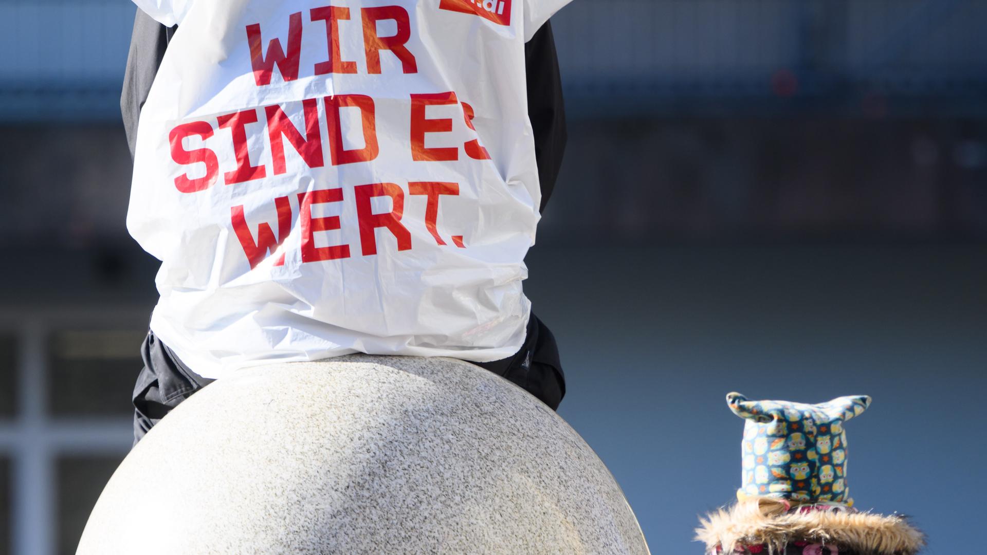 Ein Erzieher sitzt auf einem Stein. Er trägt eine Streikweste aus Plastik, auf der steht "Wir sind es wert". Ein Erzieher sitzt auf einem Stein. Er trägt eine Streikweste aus Plastik, auf der steht "Wir sind es wert".