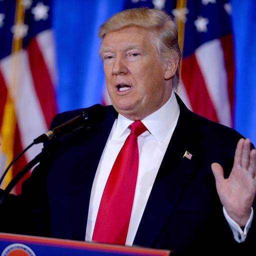 Donald Trump steht hinter einem Rednerpult und streckt die Hände nach oben.