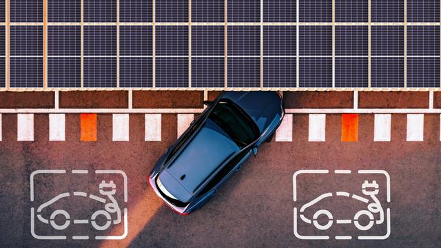 Ein Elektroauto fährt an eine Ladestation heran, die von Solarzellen überdacht ist. Die Aufnahme ist aus der Luft entstanden.