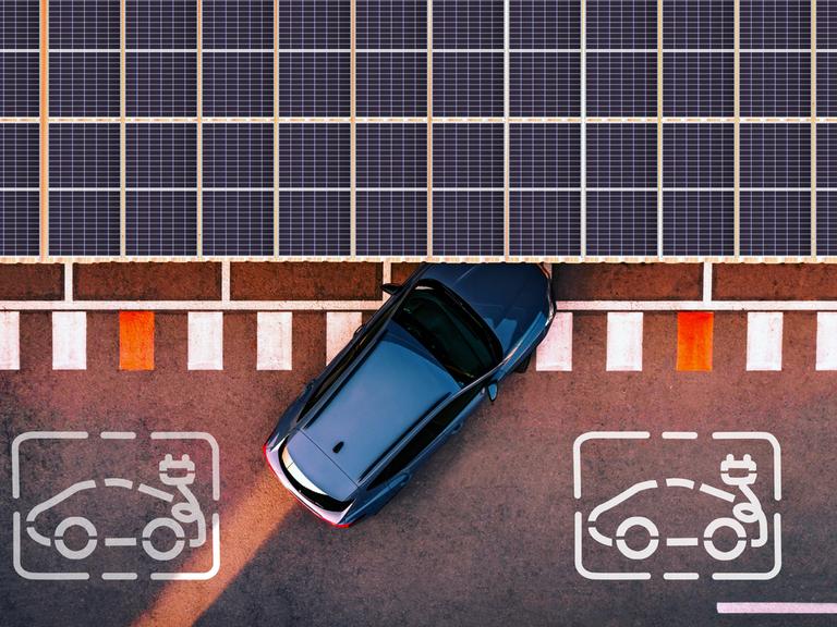 Ein Elektroauto fährt an eine Ladestation heran, die von Solarzellen überdacht ist. Die Aufnahme ist aus der Luft entstanden.