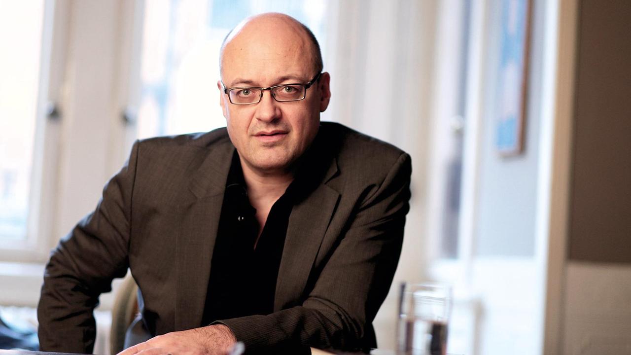 Der Autor Peter Michalzik. Er trägt Glatze, ein Metallbrillengestell, schwarzes Hemd und ein dunkles Sakko und blickt frontal in die Kamera. Der Autor Peter Michalzik. Er trägt Glatze, ein Metallbrillengestell, schwarzes Hemd und ein dunkles Sakko und blickt frontal in die Kamera.
