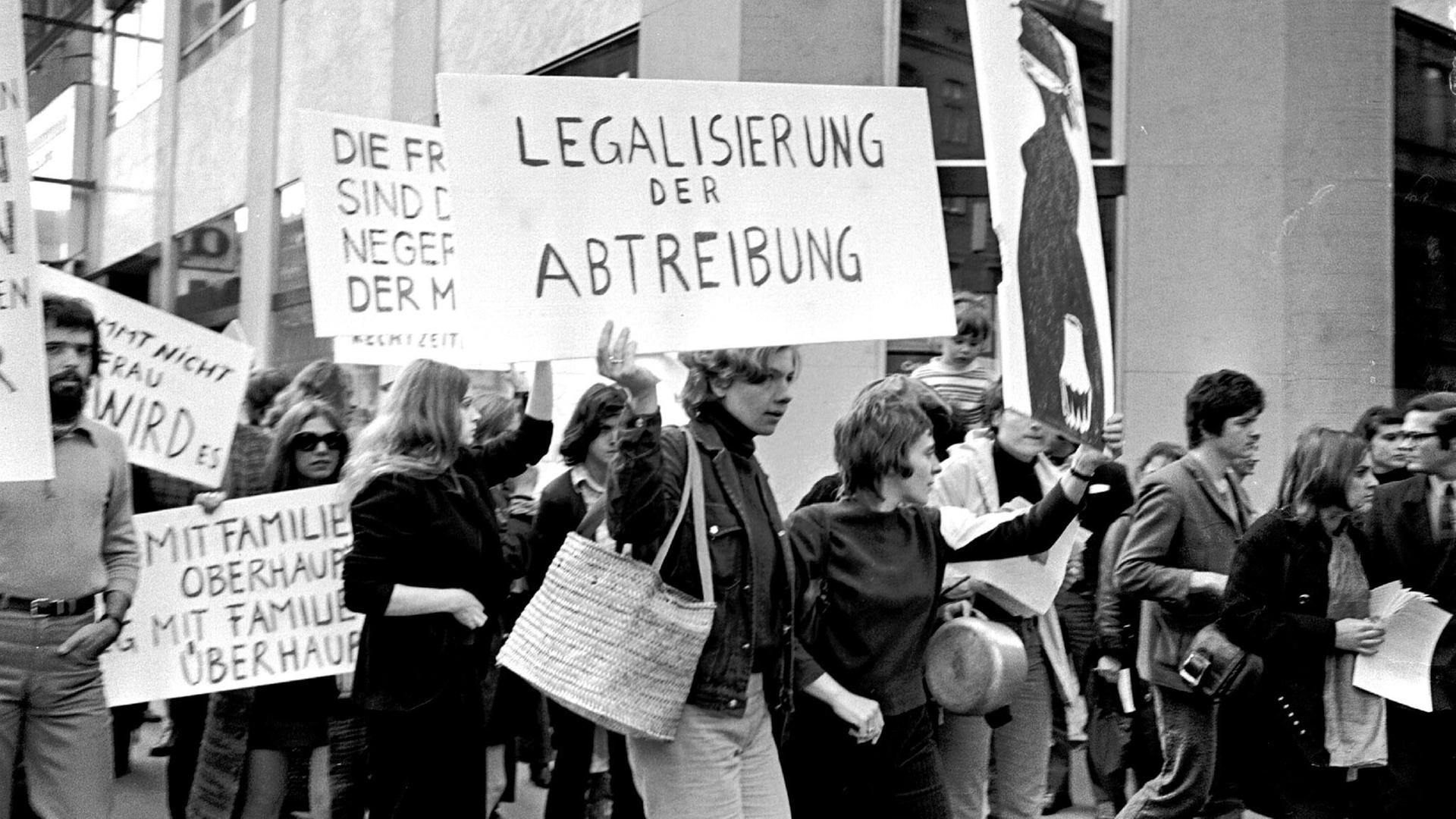 Historisches Schwarzweißfoto demonstrierender Frauen, von der eine ein Schild trägt mit der Aufschrift: "Legalisierung der Abtreibung". Historisches Schwarzweißfoto demonstrierender Frauen, von der eine ein Schild trägt mit der Aufschrift: "Legalisierung der Abtreibung".