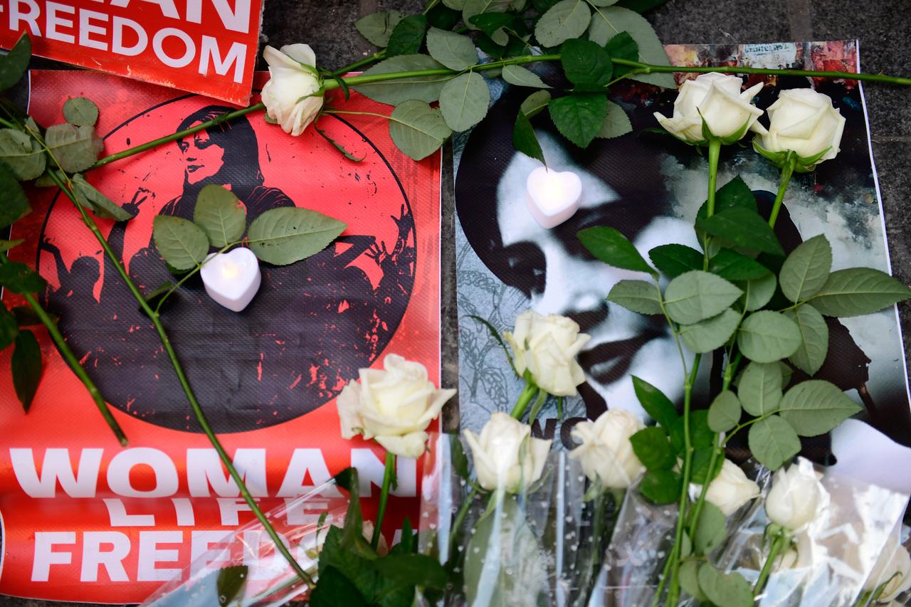 Auf dem Straßenpflaster liegen ein Transparent und ein Foto von Masha Amini. Darüber weisse Rosen.