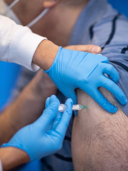 Eine Mitarbeiterin eines Impfzentrums verabreicht einem Mann eine Impfung mit dem Corona-Impfstoff.