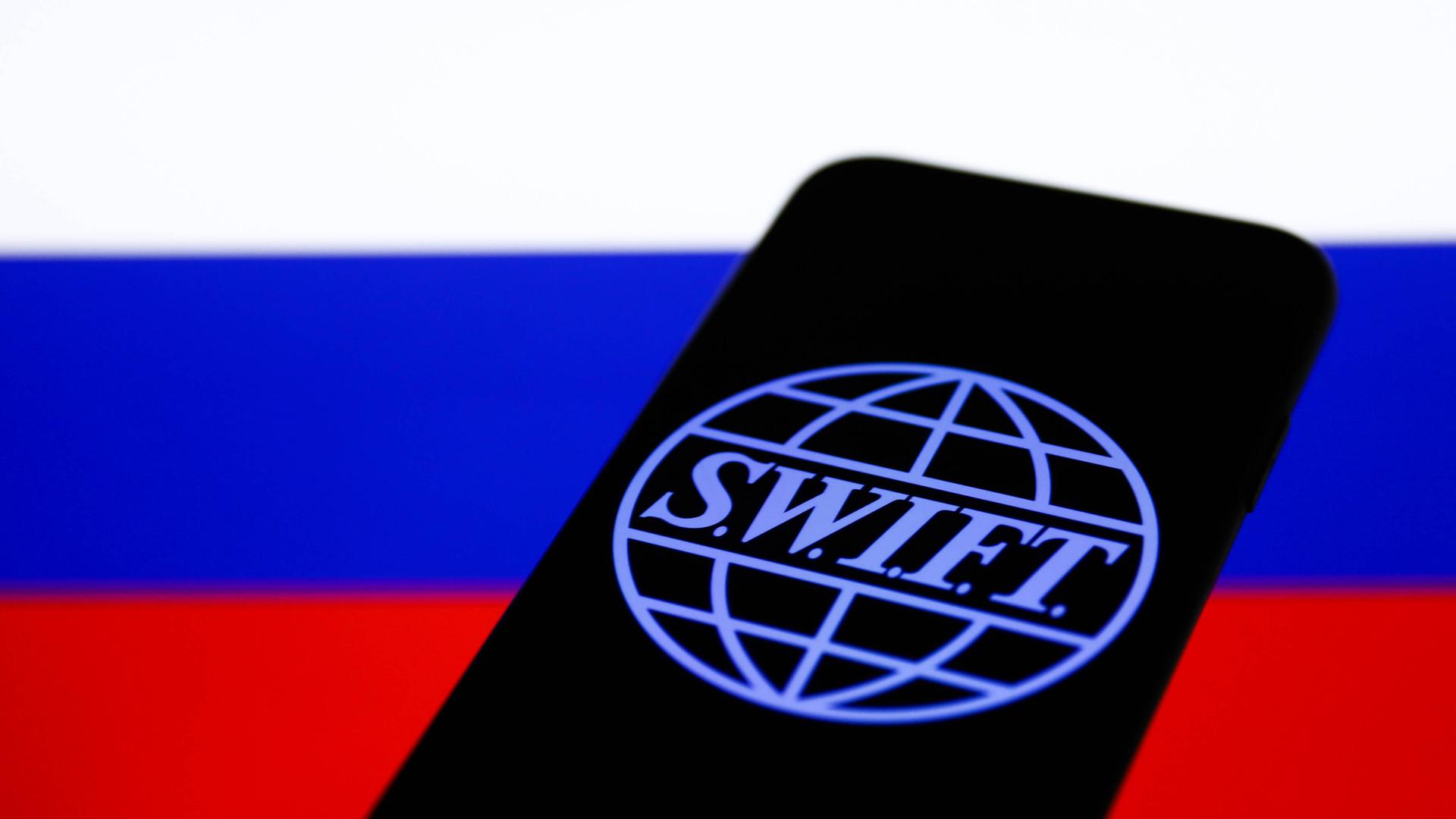 SWIFT-Logo auf einem Smartphone vor russischer Flagge SWIFT-Logo auf einem Smartphone vor russischer Flagge