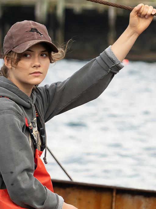 Schauspielerin Emilia Jones sitzt in einer Szene des oscarprämierten Films "Coda" in Arbeitskleidung einem Fischerboot und schaut in die Kamera.