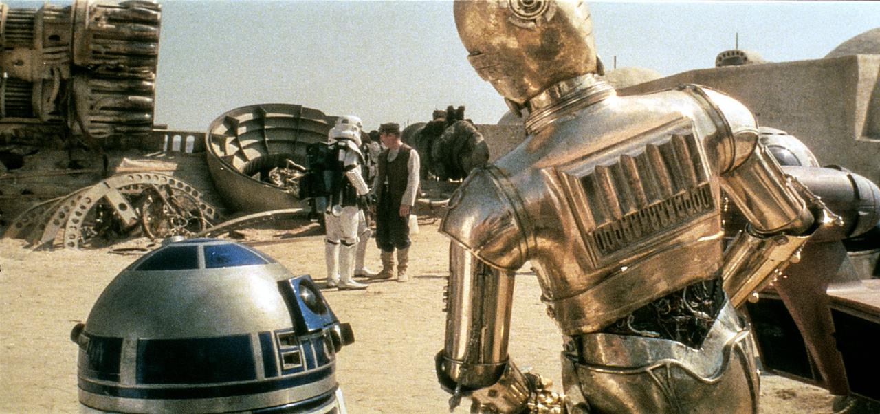 Im Filmstill aus "Star Wars Episode IV - Eine neue Hoffnung" beobachten die Droiden C3PO und R2D2 einen Stormtrooper.