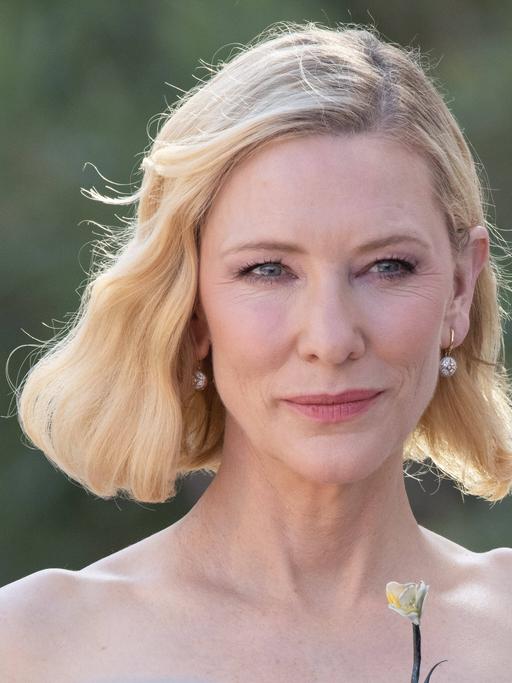Cate Blanchett steht in einer grünen Landschaft und lächelt.
