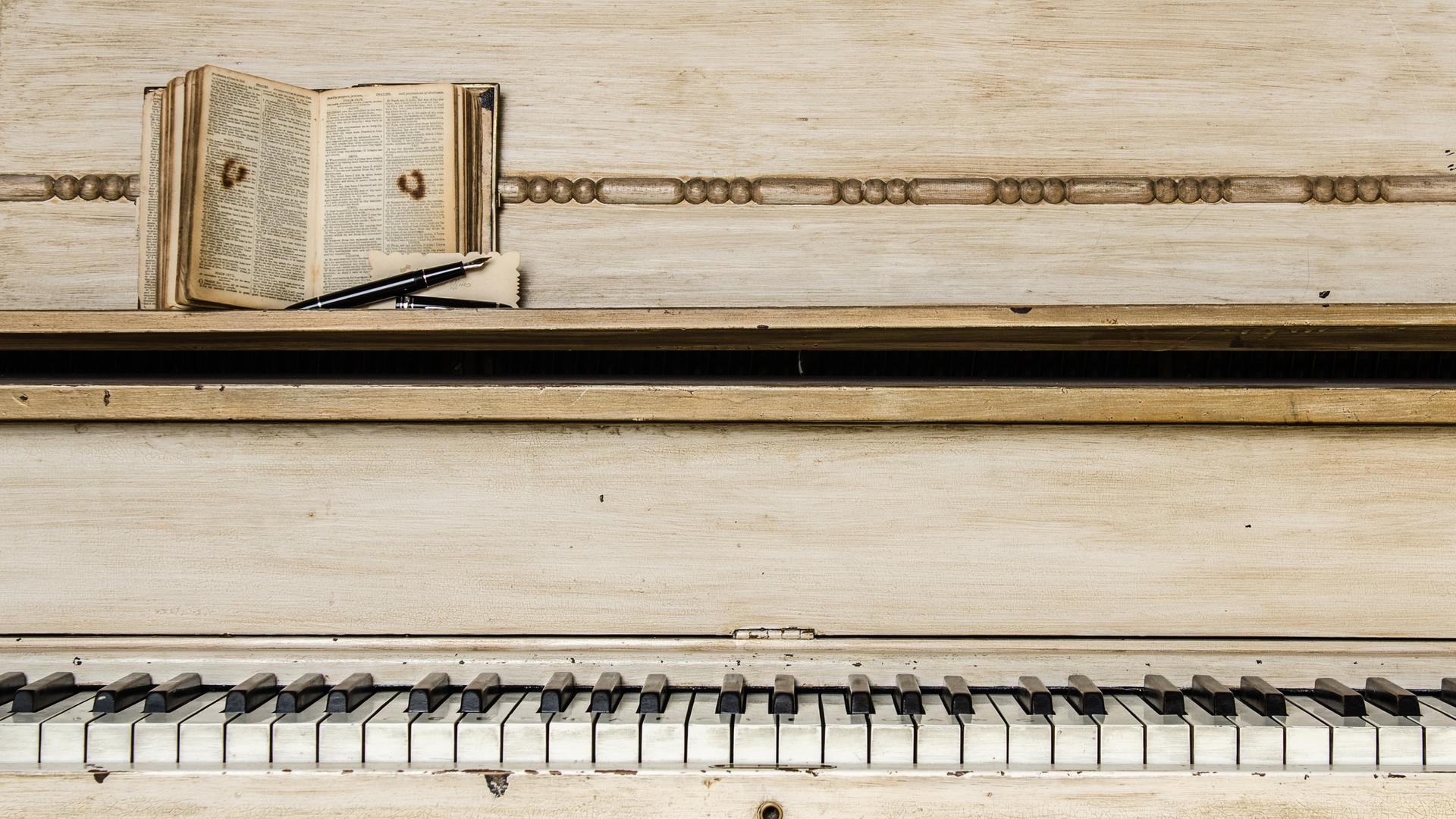 Musik hat eine besondere Anziehungskraft auf Schriftsteller und Autorinnen. Zu sehen ist ein Klavier mit heruntergespielten Tasten, auf der Ablage liegt eine Bibel oder ein ähnliches Buch mit klein geschriebenem Text. Musik hat eine besondere Anziehungskraft auf Schriftsteller und Autorinnen. Zu sehen ist ein Klavier mit heruntergespielten Tasten, auf der Ablage liegt eine Bibel oder ein ähnliches Buch mit klein geschriebenem Text.