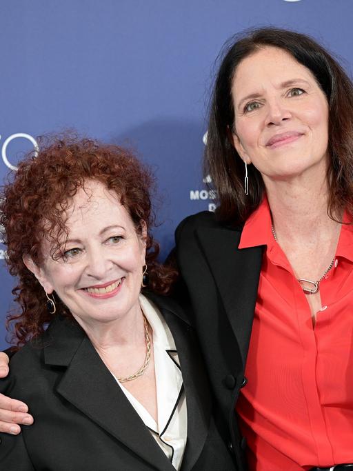 Laura Poitras und Nan Goldin stehen Arm in Arm vor einer Fotowand