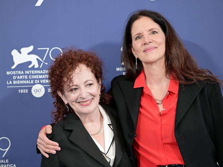 Laura Poitras und Nan Goldin stehen Arm in Arm vor einer Fotowand