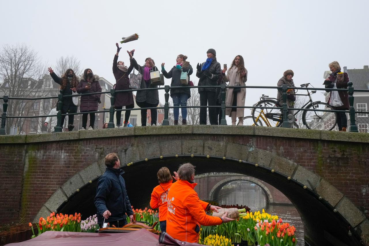 Ein Boot voller Tulpen fährt durch eine Gracht, Menschen auf einer Brücke fangen hochgeworfene Blumensträuße. Ein Boot voller Tulpen fährt durch eine Gracht, Menschen auf einer Brücke fangen hochgeworfene Blumensträuße.