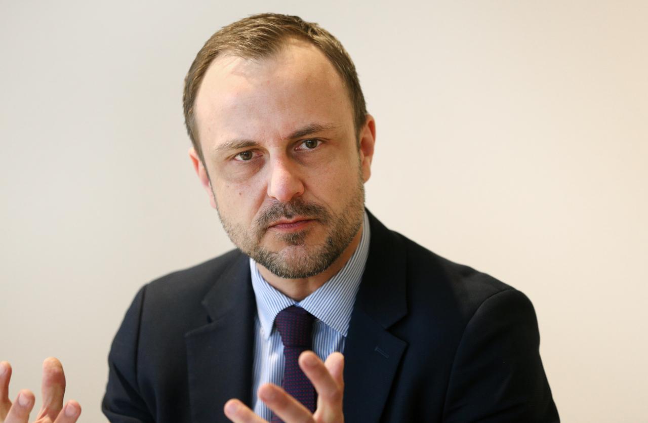 Porträt von Peter R. Neumann auf einem Podium. Er trägt einen dunkelblauen Anzug und Krawatte und guckt ernst. Porträt von Peter R. Neumann auf einem Podium. Er trägt einen dunkelblauen Anzug und Krawatte und guckt ernst.