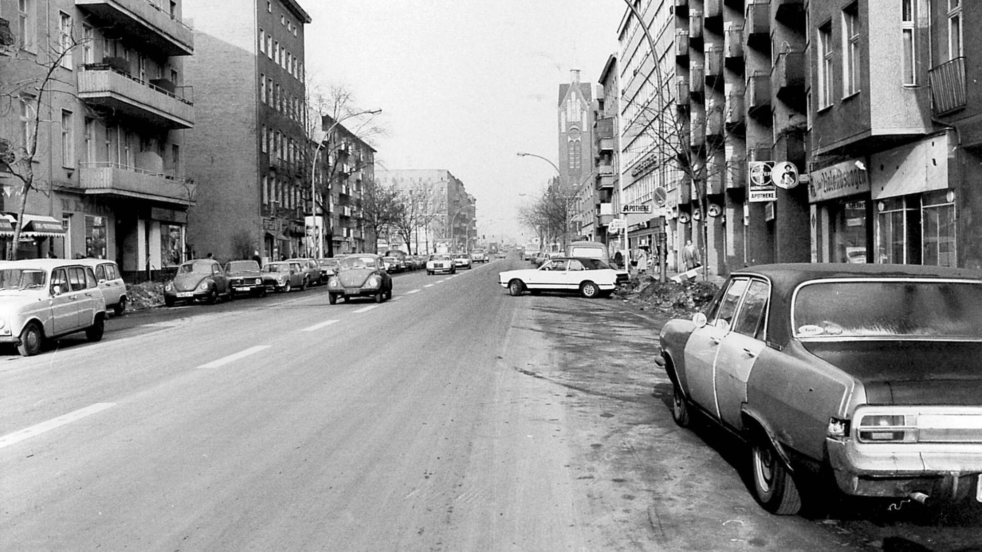 Schwarzweißaufnahme einer menschenleeren Berliner Straße mit parkenden Autos. Die Straße führt zum Fluchtpunkt des Bildes.