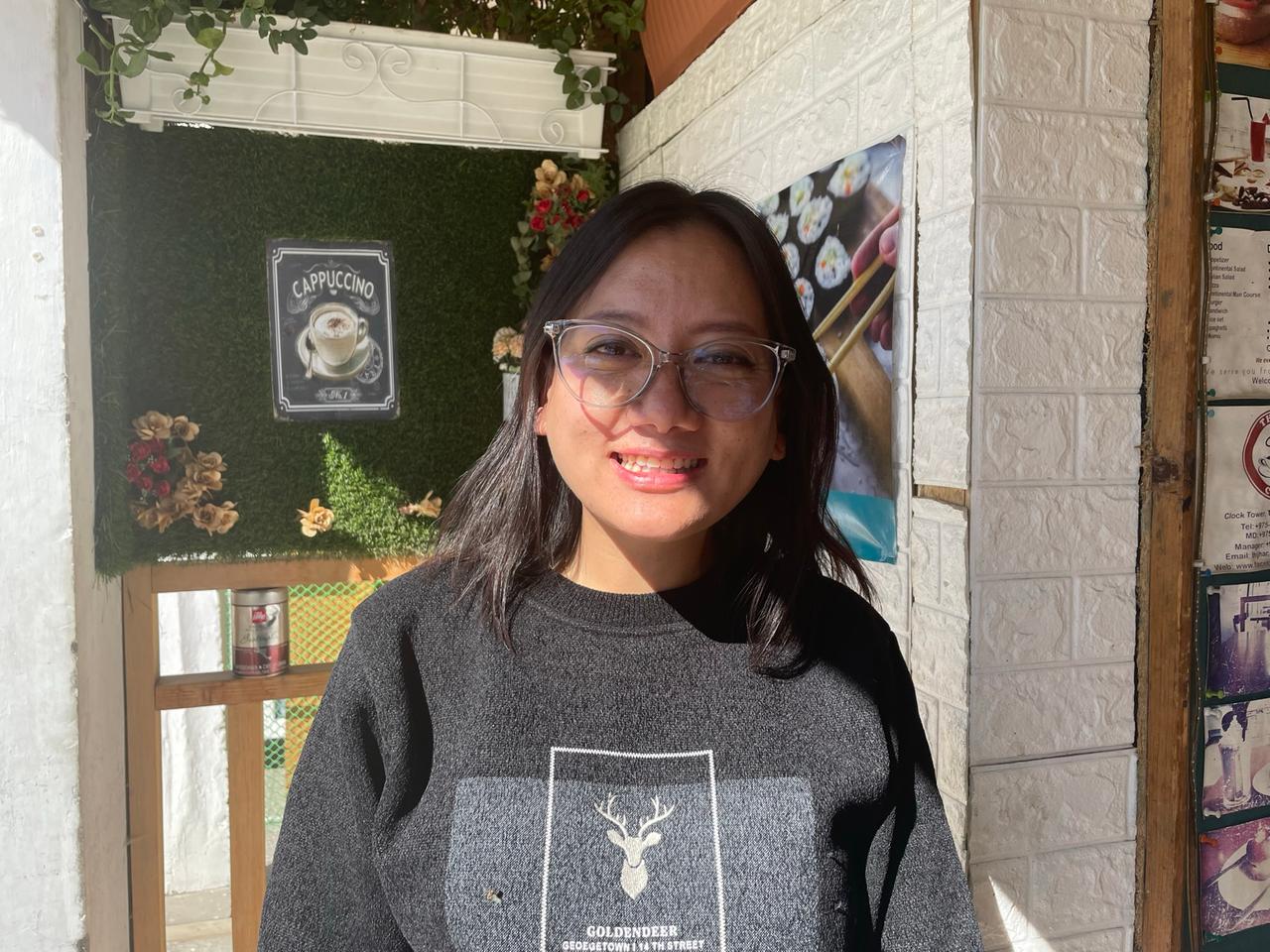 Eine junge Frau mit Brille und Pulli steht in einem Café.