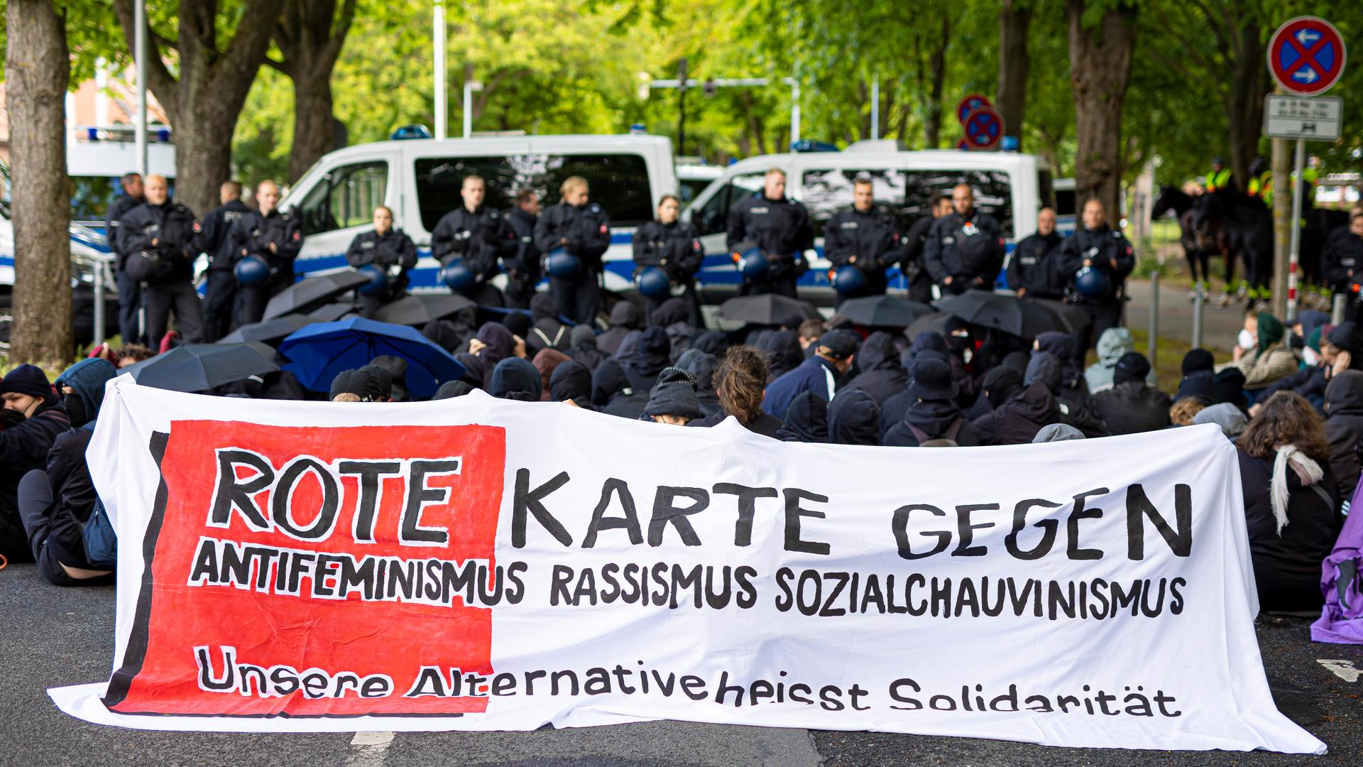 Demonstranten halten eine Sitzblockade ab und haben ein Banner mit folgender Aufschrift aufgespannt: "Rote Karte gegen Antifeminismus Rassismus Sozialchauvinismus - unsere Alternative heißt Solidarität"