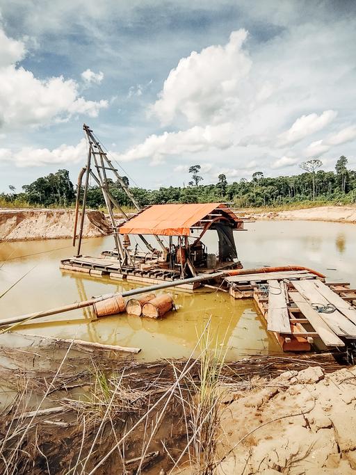 An einem Wasserloch, steht auf einem überdachten Holzfloss ein Motor an dem ein langer Schlauch angebracht ist. 