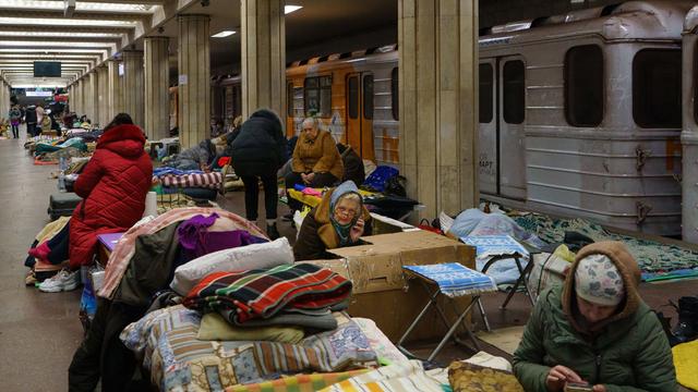 Menschen in Charkiw mit Decken und Taschen in einer U-Bahn-Station. Dahinter steht ein Zug.