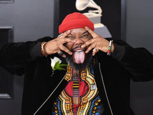 Der Musiker Kokayi hält sich auf der Grammy-Verleihung die Finger vors Gesicht und streckt die Zunge raus.