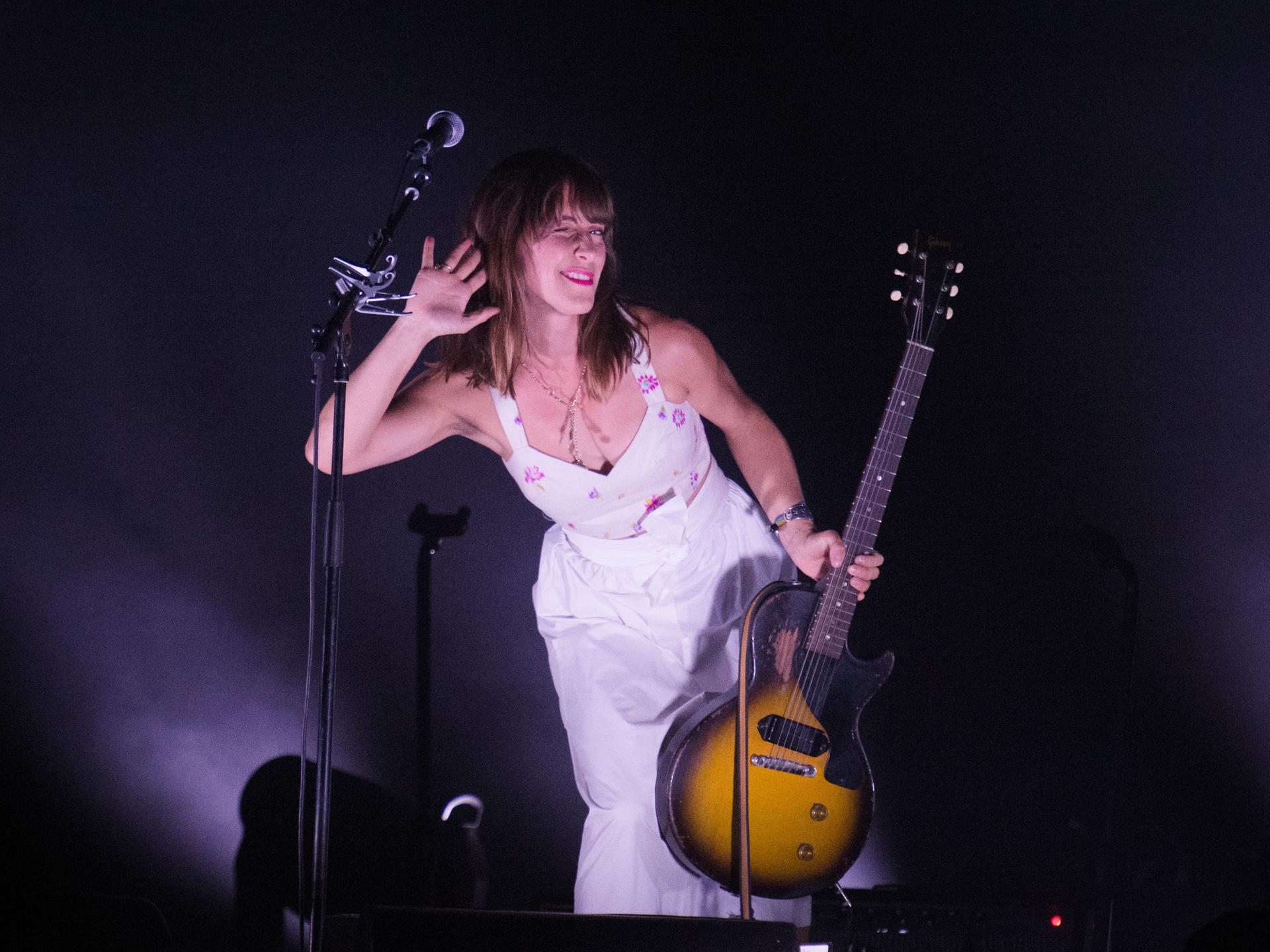 Die Feist steht mit ihrer Gitarre neben einem Mikrofon auf der Bühne.