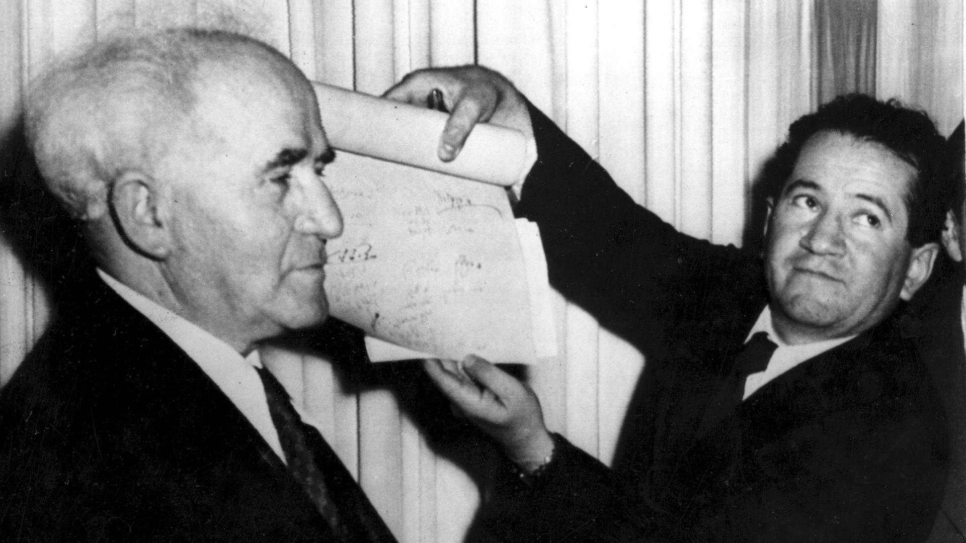 Ein Mann hält das Dokument hoch, mit dem die Gründung des Staates Israel proklamiert wird. Premierminister David Ben-Gurion steht am 14. Mai 1948 links neben dem Mann