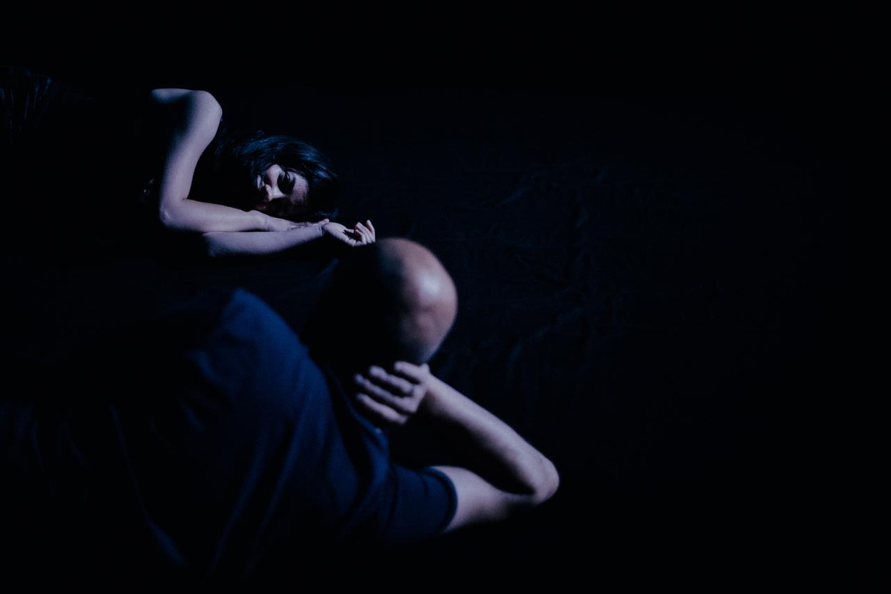 Zwei Personen in einem dunklen Raum, sichtbar von hinten ein Mann, sichtbar von vorn eine Frau.
