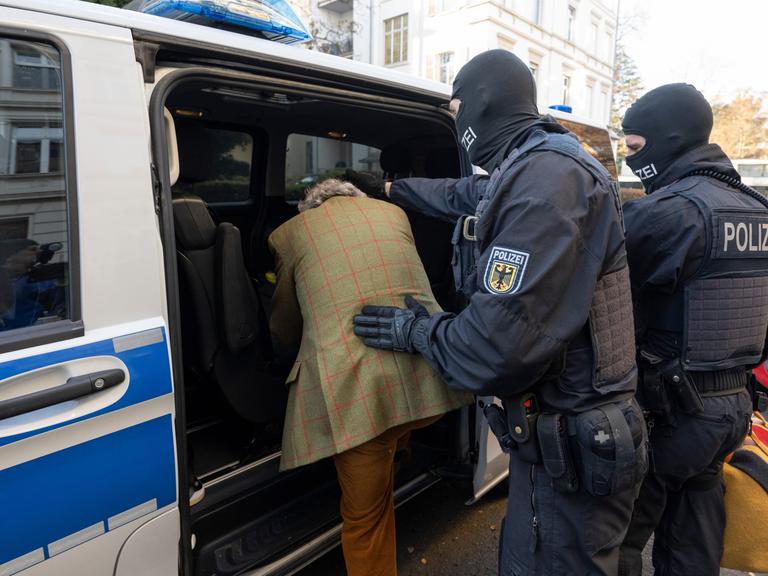 Frankfurt/Main: Bei einer Razzia gegen sogenannte "Reichsbürger" führen vermummte Polizisten nach der Durchsuchung eines Hauses einen festgenommenen Verdächtigen zu einem Polizeifahrzeug.