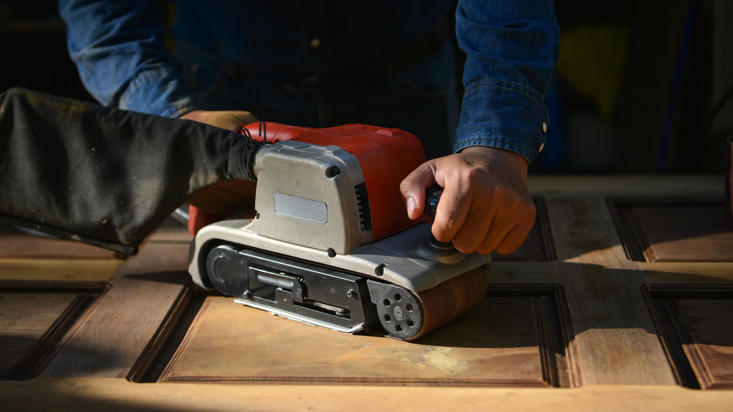 Eine Holztür wird abgeschmirgelt.