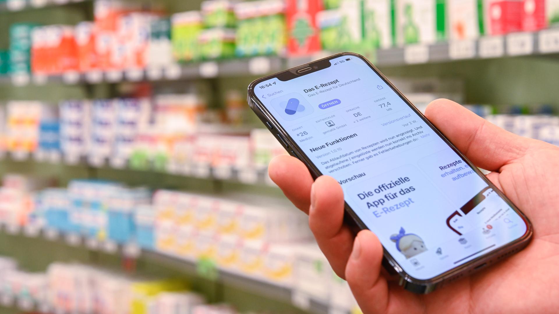 Jemand hält in einer Apotheke ein Smartphone in der Hand, auf dessen Display eine App zur Verarbeitung von E-Rezepten geöffnet ist. Jemand hält in einer Apotheke ein Smartphone in der Hand, auf dessen Display eine App zur Verarbeitung von E-Rezepten geöffnet ist.