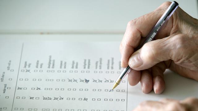 Eine Hand hält einen Kugeschreiber und kreuzt auf einem Fragebogen Antwortmöglichkeiten an.
