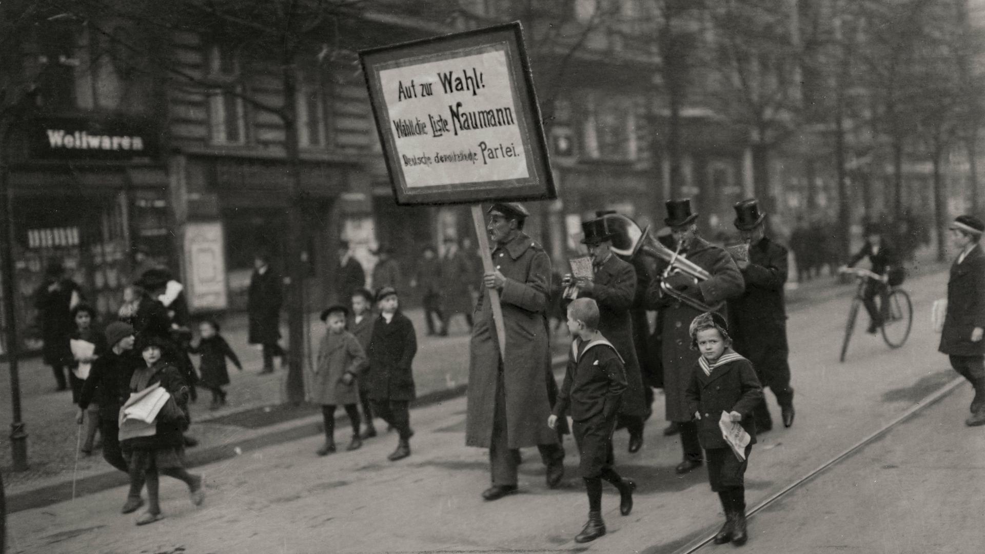 Wahlumzug der DDP. Ein Mann trägt ein Plakat mit der Aufschrift: "Auf zur Wahl! Wählt die Liste Naumann, Deutsche Demokratische Partei". Wahlumzug der DDP. Ein Mann trägt ein Plakat mit der Aufschrift: "Auf zur Wahl! Wählt die Liste Naumann, Deutsche Demokratische Partei".