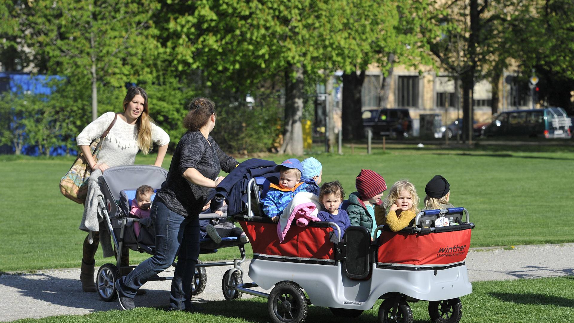 Zwei Frauen schieben kleine Kinder in einem großen und einem kleinen Kinderwagen. Zwei Frauen schieben kleine Kinder in einem großen und einem kleinen Kinderwagen.