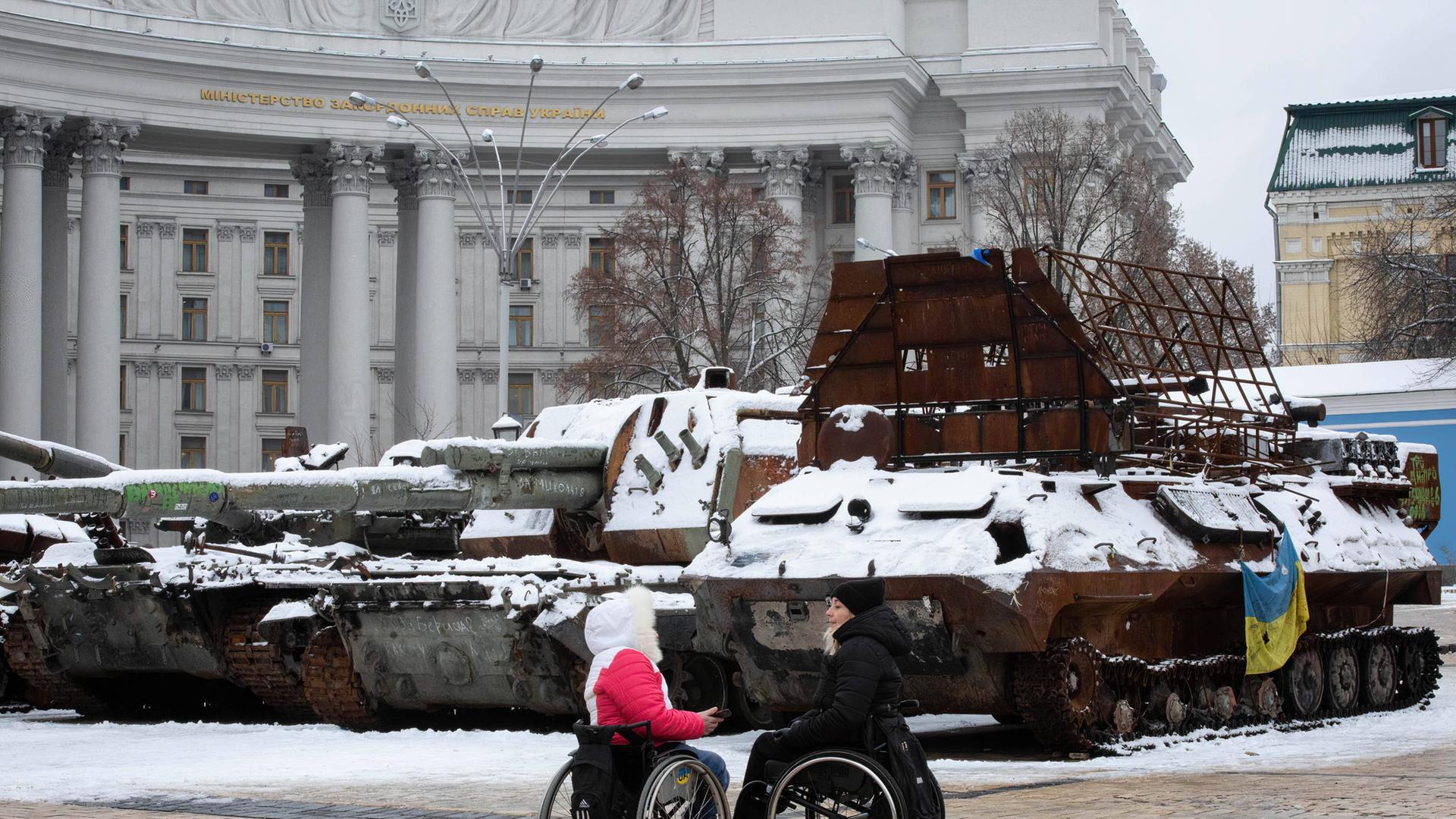 Frauen in Rollstühlen unterhalten sich in der Nähe von zerstörten russischen Panzern im Zentrum von Kiew Frauen in Rollstühlen unterhalten sich in der Nähe von zerstörten russischen Panzern im Zentrum von Kiew