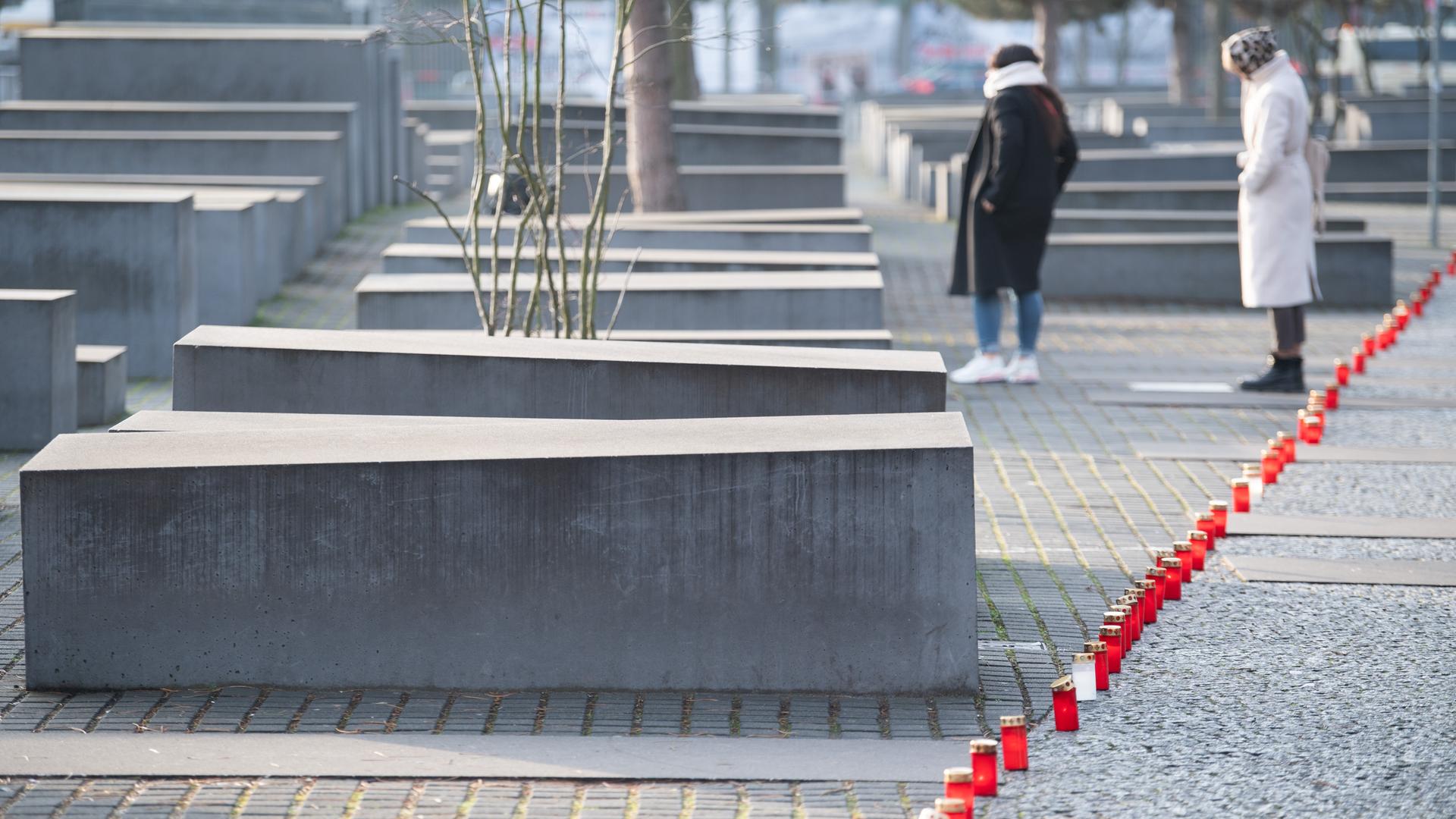 Zwei Frauen stehen neben Stelen und roten Grablichtern am Denkmal für die ermordeten Juden Europas in Berlin