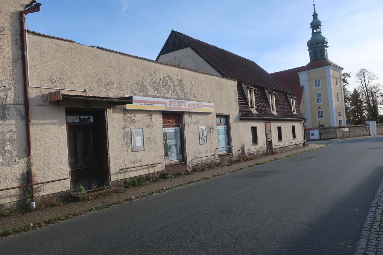 An einem verlassenen Gebäude in einem kleinen Dorf ist noch ein verblasstes Rewe-Logo zu erkennen. An einem verlassenen Gebäude in einem kleinen Dorf ist noch ein verblasstes Rewe-Logo zu erkennen.
