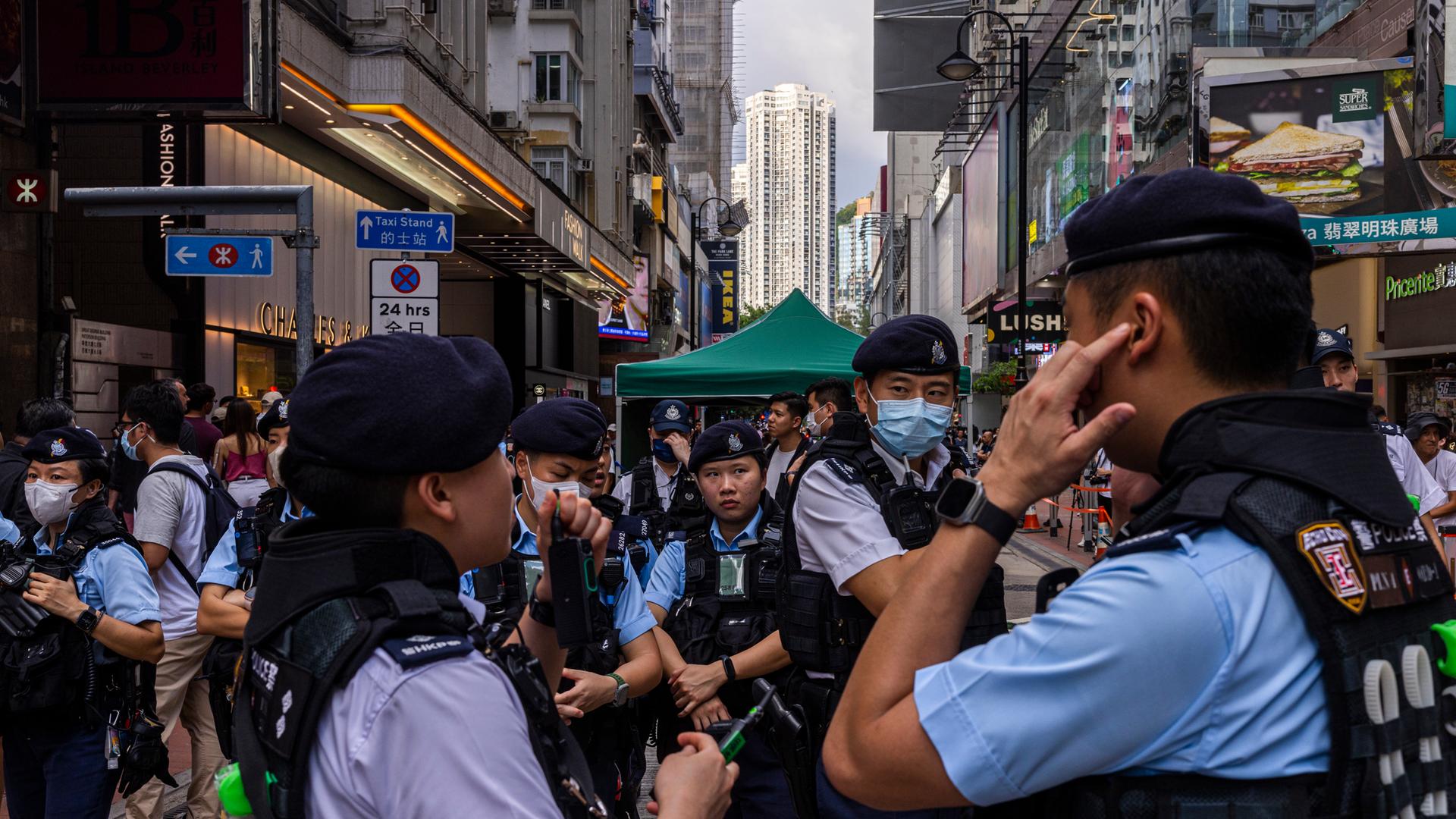 Männer und Frauen in blauen Polizeiuniformen stehen in einer Fußgängerzone, in der viele Menschen unterwegs sind.