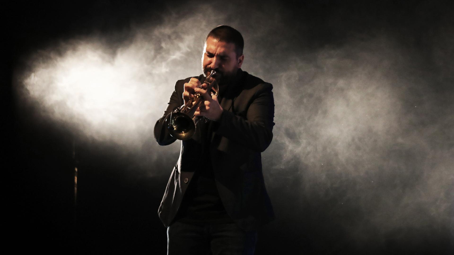 Der Musiker Ibrahim Maalouf steht im schwarzen Anzug auf einer Bühne und spielt Trompete, hinter ihm bildet weißer, angeleuchteter Rauch eine Art Wolke. Der Musiker Ibrahim Maalouf steht im schwarzen Anzug auf einer Bühne und spielt Trompete, hinter ihm bildet weißer, angeleuchteter Rauch eine Art Wolke.