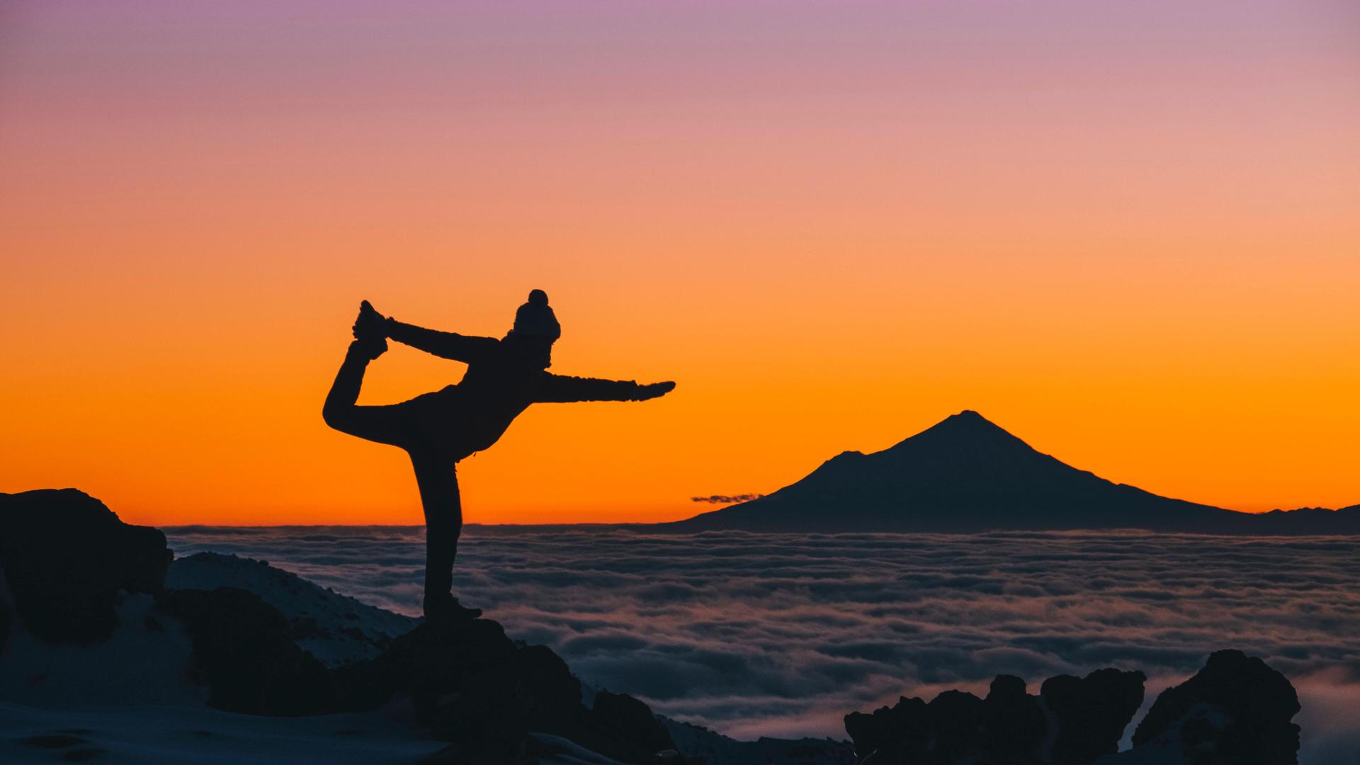 Eine junge Frau macht in Neuseeland Yogaübungen bei Sonnenuntergang über den Wolken, im Hintergrund ist der Mount Taranaki zu sehen.
Eine junge Frau macht in Neuseeland Yogaübungen bei Sonnenuntergang über den Wolken, im Hintergrund ist der Mount Taranaki zu sehen.