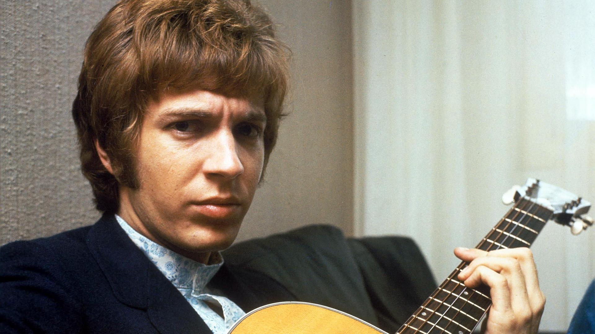 Der Musiker Scott Walker mit Gitarre. Er trägt eine Pony-Frisur, schwarzes Jackett und ein helles Hemd. Sein Blick ist ernst. Der Musiker Scott Walker mit Gitarre. Er trägt eine Pony-Frisur, schwarzes Jackett und ein helles Hemd. Sein Blick ist ernst.