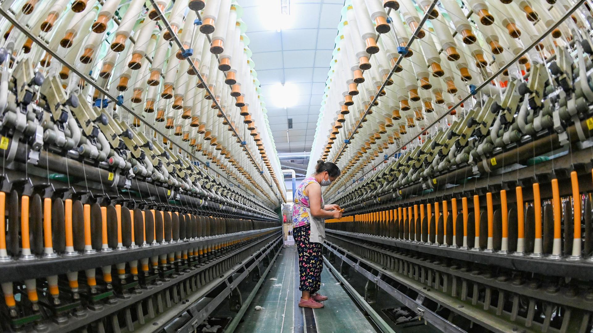 Eine Frau steht in einer Textilindustie-Anlage in China, umgeben von riesigen Maschinen.