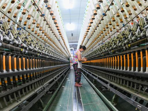 Eine Frau steht in einer Textilindustie-Anlage in China, umgeben von riesigen Maschinen.