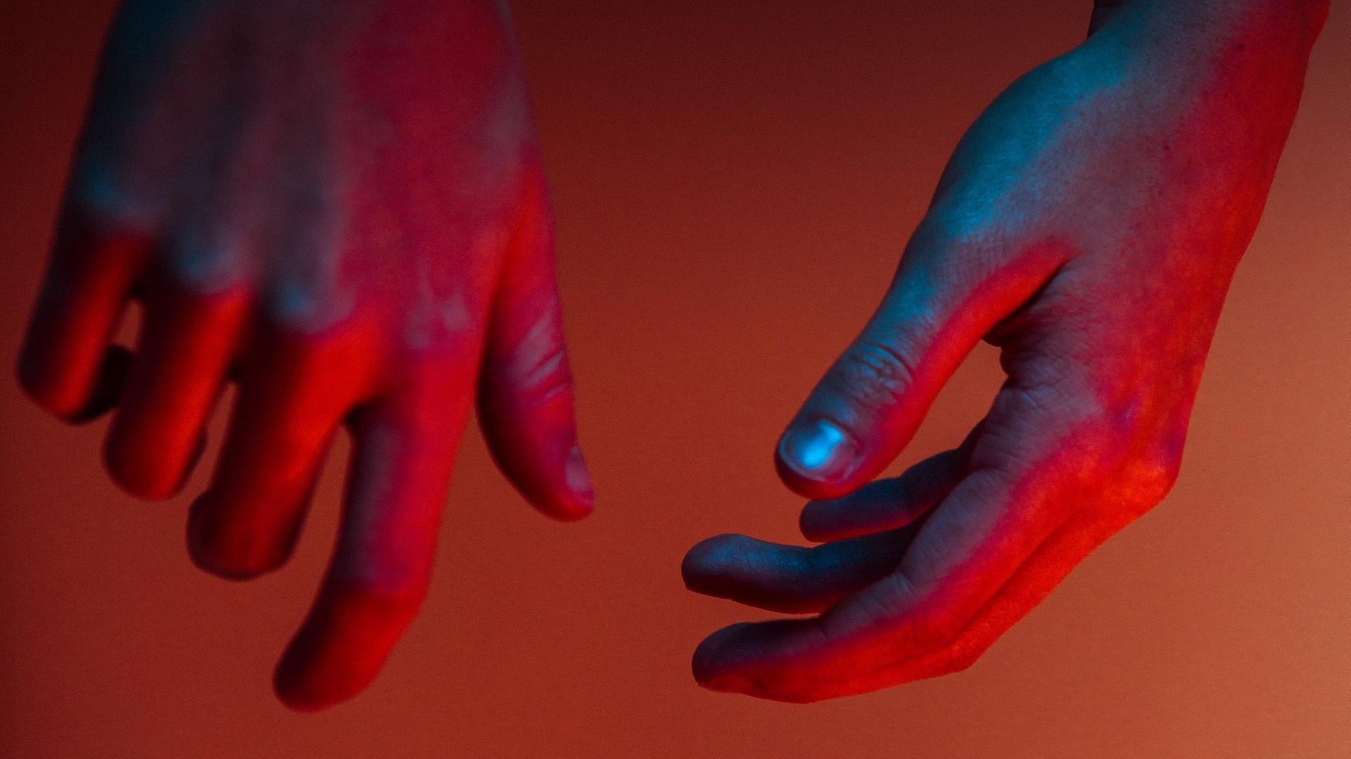 Zwei Hände, die blau, lila und rot beleuchtet sind, hängen von oben herab. Zwei Hände, die blau, lila und rot beleuchtet sind, hängen von oben herab.