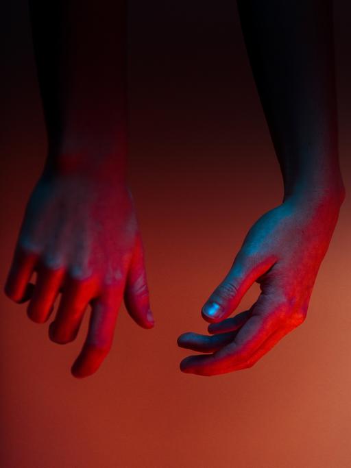 Zwei Hände, die blau, lila und rot beleuchtet sind, hängen von oben herab.