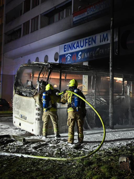 Zwei Feuerwehrmänner löschen an der Sonnenallee in Berlin einen Bus, der von Unbekannten angezündet worden war. 
