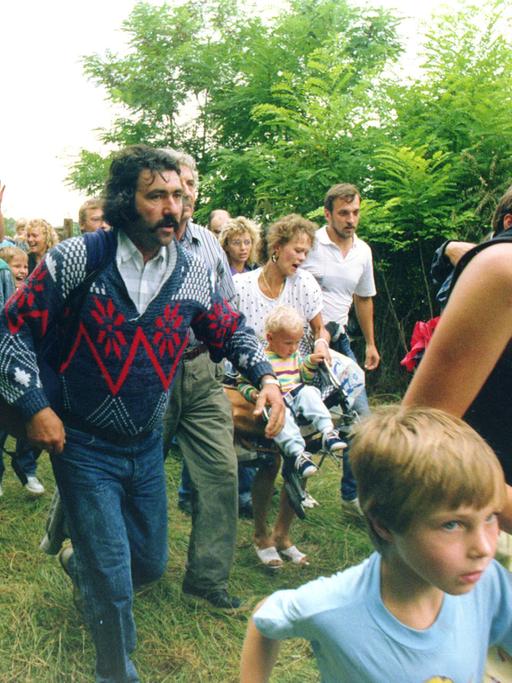Mehrere Hundert DDR-Bürger rennen am 19. August 1989 im Laufschritt durch ein Holztor über die ungarisch-österreichische Grenze nach Mörbisch auf der oesterreichischen Seite.